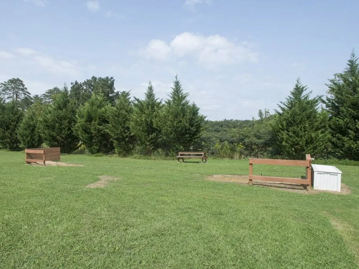 A peaceful green space with benches, expansive grassy areas, mature trees, and distant scenic views. The setting is ideal for picnics, nature watching, and casual family gatherings in the outdoors.