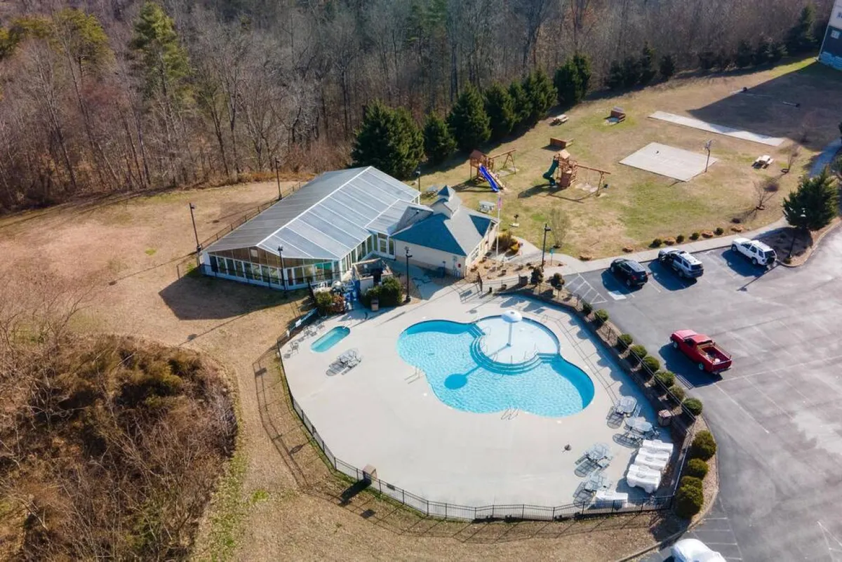 This exterior image captures a vibrant scene featuring a large swimming pool, a recreational building, and a playground area. The playful atmosphere is accentuated by children’s activities and the inviting setting for family gatherings.