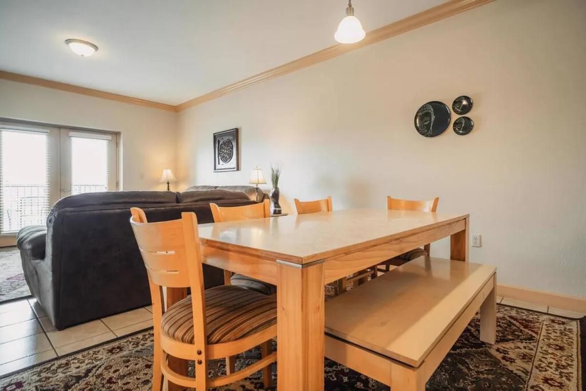 This interior shot showcases a warm, inviting dining table adjacent to a seating area, with decorative wall plates and a textured floor rug adding homely charm. The arrangement is ideal for family dinners, casual gatherings, or engaging game nights, aligning well with the theme of memorable shared experiences.
