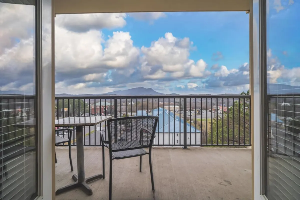 This inviting balcony scene features a sturdy railing overlooking a sweeping mountain view, with a set of table and chairs for outdoor dining or conversation. The mood is tranquil yet social, ideal for morning coffee or evening gatherings under the stars.