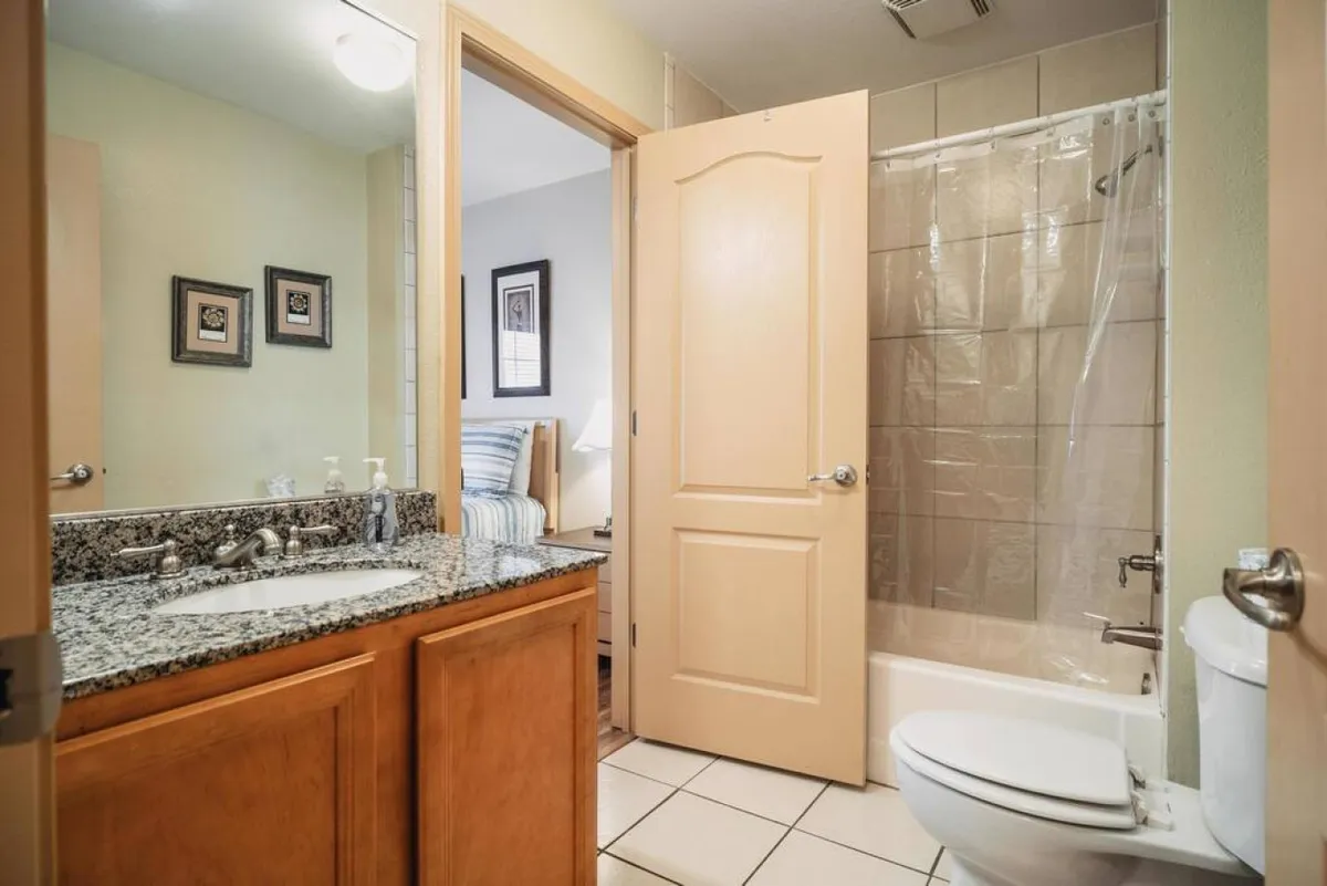 A tranquil bathroom space with a granite countertop, large mirror, and a glimpse of the shower area. The natural light and uncluttered surfaces evoke a sense of freshness and readiness for restful routines.