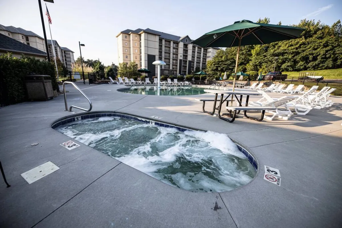 This image depicts the resort's outdoor amenities, including a sparkling swimming pool, a bubbling hot tub, lounge chairs arranged for sunbathing, a shaded area with an umbrella, and a picnic table nearby. The setting is lively yet relaxed, ideal for gatherings ranging from morning swims to evening picnics.